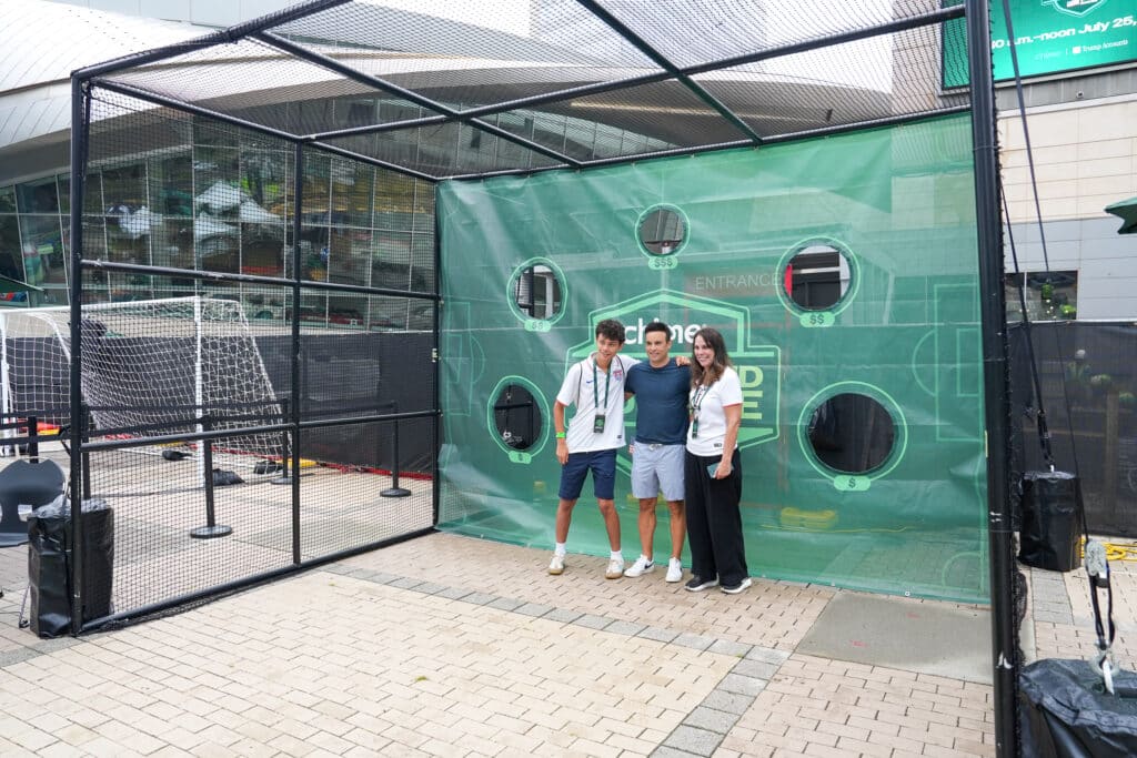 Three guests posing at a branded soccer target cage at an outdoor sponsor activation in Charlotte