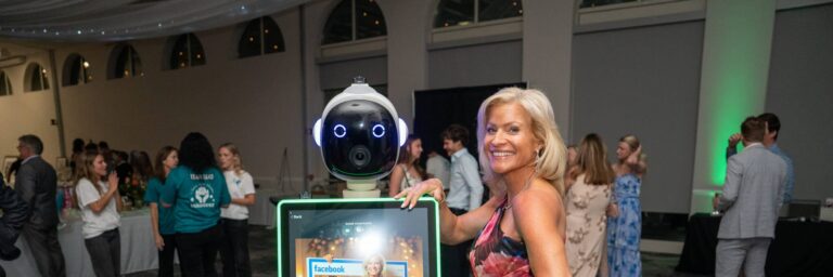 Rosie the AI photo booth robot at a gala event, with a smiling woman posing beside it, showcasing interactive technology and guest engagement in a lively setting.