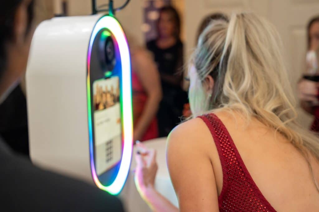 A guest in a sequined dress standing at the glam booth touchscreen, reviewing her photo on the ring-lit display